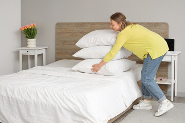 Wall Mural - Pretty young woman putting pillows on bed in modern bedroom