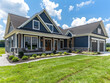  A photo of the exterior front view of an off white and navy blue craftsman style home with dark grey accents, in middle America on green grass, with clouds overhead. Created with Ai