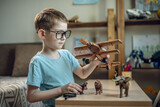 Fototapeta  - A child boy in the children's room is playing with a toy wooden airplane with animals of the savannah. Fantasies of great adventures and travels