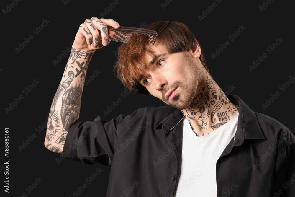 Young tattooed barber combing hair on dark background, closeup