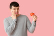 Young man with tomato suffering from toothache on pink background