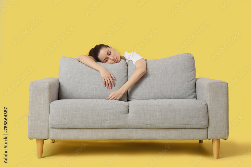 Tired young woman resting on sofa against yellow background