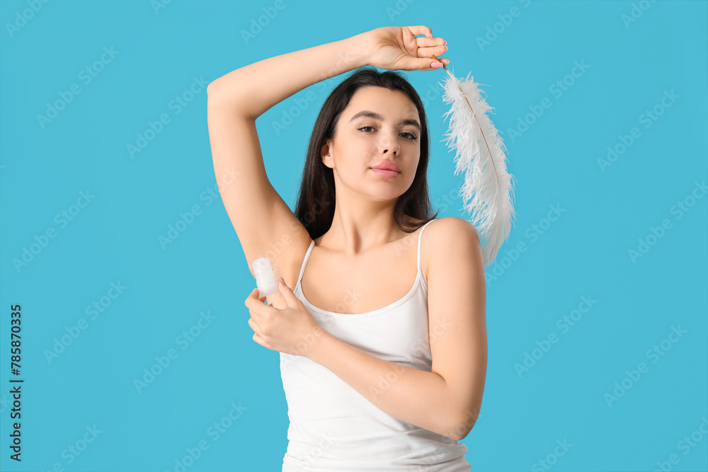 Beautiful young woman with crystal deodorant and feather on blue background