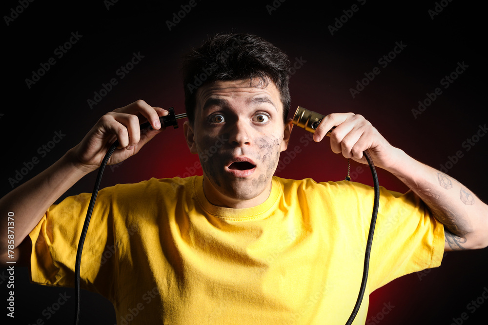 Electrocuted young man with burnt face and plug on dark background, closeup