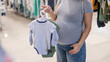 Caucasian pregnant woman chooses baby clothes in a store. Faceless expectant mother in the 3rd trimester. 