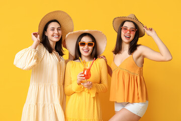 Wall Mural - Beautiful young women in wicker hats with glass of cocktail on yellow background. Summer party