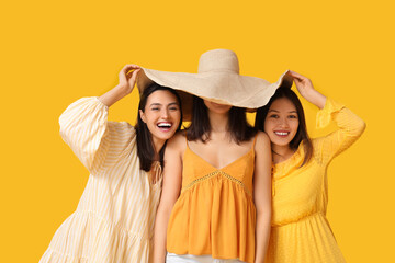 Wall Mural - Beautiful young women with wicker hat on yellow background. Summer party