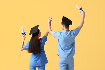 Wall Mural - Medical graduate couple with diplomas on yellow background, back view