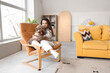 Young woman with cute poodle sitting in armchair at home