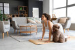 Sporty young woman with cute poodle doing yoga at home