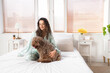Young woman with cute poodle sitting in bedroom