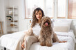 Young woman with funny poodle sitting in bedroom