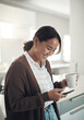 © peopleimages.com - Phone, smile and Asian woman drinking coffee in kitchen at home for breakfast in the morning. Smartphone, tea cup and happy person on social media, internet search and reading email on mobile app