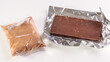Chocolate bar unfolded in foil sheath. Cocoa and chocolos on white background, concept of price increase for raw materials of chocolate production.