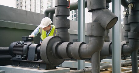 Wall Mural - A Engineer man looking inspecting maintenance insulated pipelines valve pump control on the roof at an industrial site. He is wearing a hard hat and safety vest