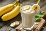 Fototapeta Do pokoju - Banana smoothie in a tall glass with sliced bananas on a wooden background