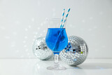 Fototapeta Tulipany - Blue cocktail with straws in glass and disco balls on white background