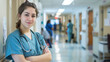 © amila - Happy joyful female medical person doctor standing in hospital corridor, arms crossed and people working in background