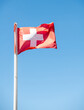 Red Switzerland national flag on pole waving against clear blue sky