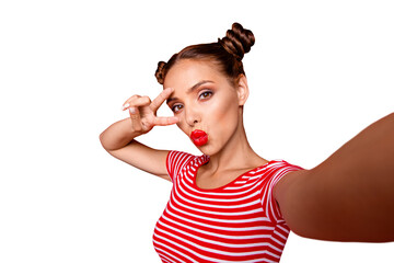 Wall Mural - Pretty cheerful girl with pouted lips shooting selfie and holding two fingers near eyes showing v-sign isolated on red background