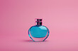 horizontal image of a round blue perfume bottle on a pink neutral background