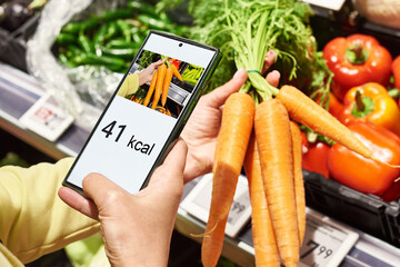 Wall Mural - Checking calories on carrot vegetable with smartphone