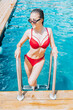 Beautiful happy young woman in red swimsuit comes out of the pool. Vertical photography.