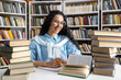 © Liubomir - A cheerful young woman with glasses and curly hair studies among stacks of books in a library, exuding curiosity and enthusiasm.