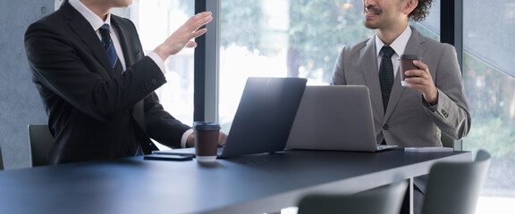 Wall Mural - Two men meeting at a computer by a window Banner of a subordinate making a proposal for a project or job and his boss listening Banner without a face