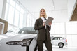 Professional smiling female car dealer posing at auto showroom holding tablet pc. Happy saleswoman working at automobile dealership, copy space. Professionalism, management concept.