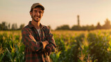 Fototapeta  - A young farmer stands with his arms crossed and smiling in the corn field in the morning.