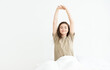 Waking up from a nap of a beautiful young woman sitting on white linens, holding her hands up. Bright room is flooded with morning light. Perfect blank for advertising mattresses or bedding products.