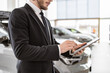 Cropped view of young car salesman in suit holding digital tablet. Confident bearded man makes an order for the purchase of a new car using modern gadgets.