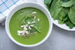 Bowl of spinach soup topped with feta cheese, horizontal shot on a grey granite background, elevated view