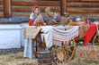 A beautiful Russian girl in traditional Russian clothes and a kokoshnik stands at a table with various national dishes near a wooden house. Festive farewell to winter.