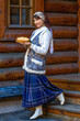 A young woman is dressed in national Russian dress. She is holding a plate of pancakes and a wicker basket in her hands. Greets guests for Maslenitsa.