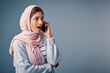 Canvas Print - Surprised, phone call and muslim woman with smartphone in studio for shock, wow or omg reaction on blue background. Hijab, amazed and Arab person with wtf expression for gossip, fake news or secret