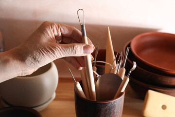 Wall Mural - Woman taking clay crafting tool from cup in workshop, closeup