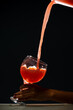 Guava juice falling from a plastic container into a glass cup held by a hand. Isolated on dark background.