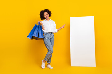 Poster - Full length body size view of attractive cheery girl holding bags new offer showing copy space isolated over bright yellow color background