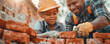 © LeManna - Father and son in helmets putting red bricks to wall at construction. Family togetherness and relationship concept.