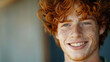 Close-up of a young man with curly red hair and freckles smiling