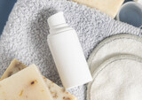 Fototapeta Boho - White blank cosmetic bottle on grey folded towel near soap bars in bathroom, mockup
