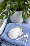 Fototapeta Boho - Opened cream jar on blue towels near basin and green monstera in bath, lid mockup