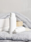 Fototapeta Boho - White one pump cosmetic bottles on grey folded towel near basin in bathroom, mockup