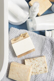 Fototapeta Boho - Soap bar with blank label on grey towel near cosmetics in bathroom top view, mockup