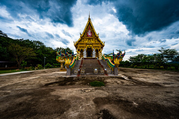 Chachoengsao, Thailand, 28 July 2023. Traditional Thai temple adorned with intricate designs and golden embellishments. Two colorful serpent statues flank the temple’s stairway entrance.