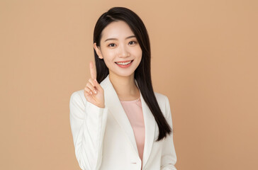 A beautiful Asian woman in a white suit, pink top and black hair is smiling while pointing to the side with one finger up