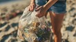 A volunteer holding a plastic bag filled with collected beach trash in their hands
