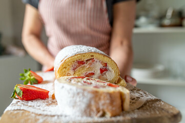 Wall Mural - Woman serving a fresh baked swiss roll filled with whipped cream and strawberries. Delicious strawberry cake